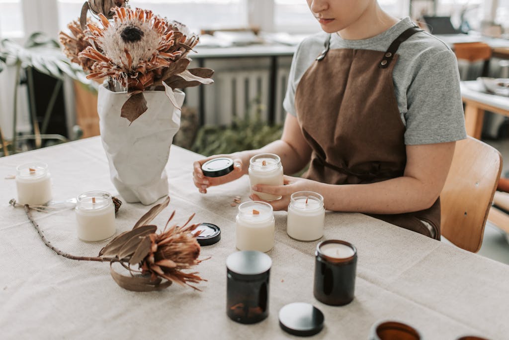 Artisan creating candles in a workshop filled with flowers and jars.